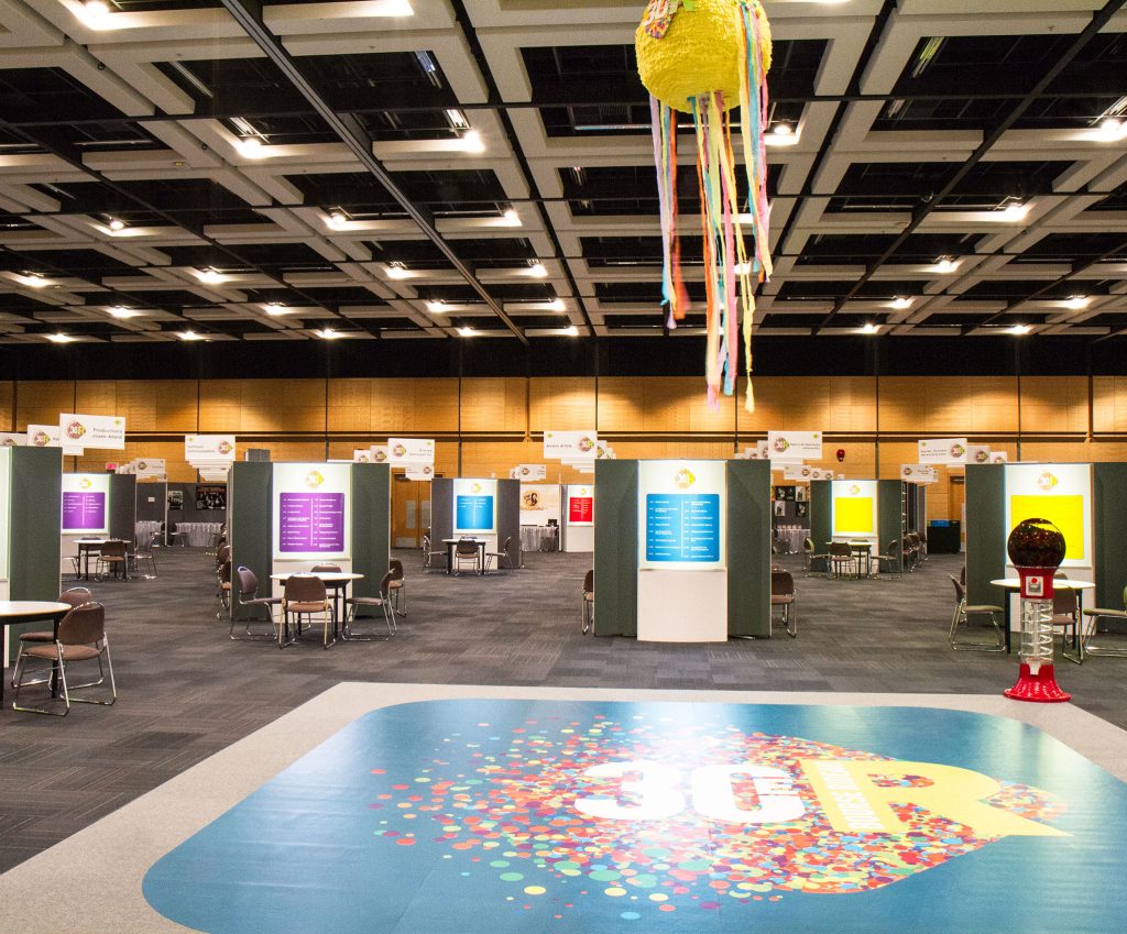 Poster session at the Québec City Convention Centre with coloful posters and a 30 Rideau logo on the floor. A yellow pinata is hung from the ceiling.