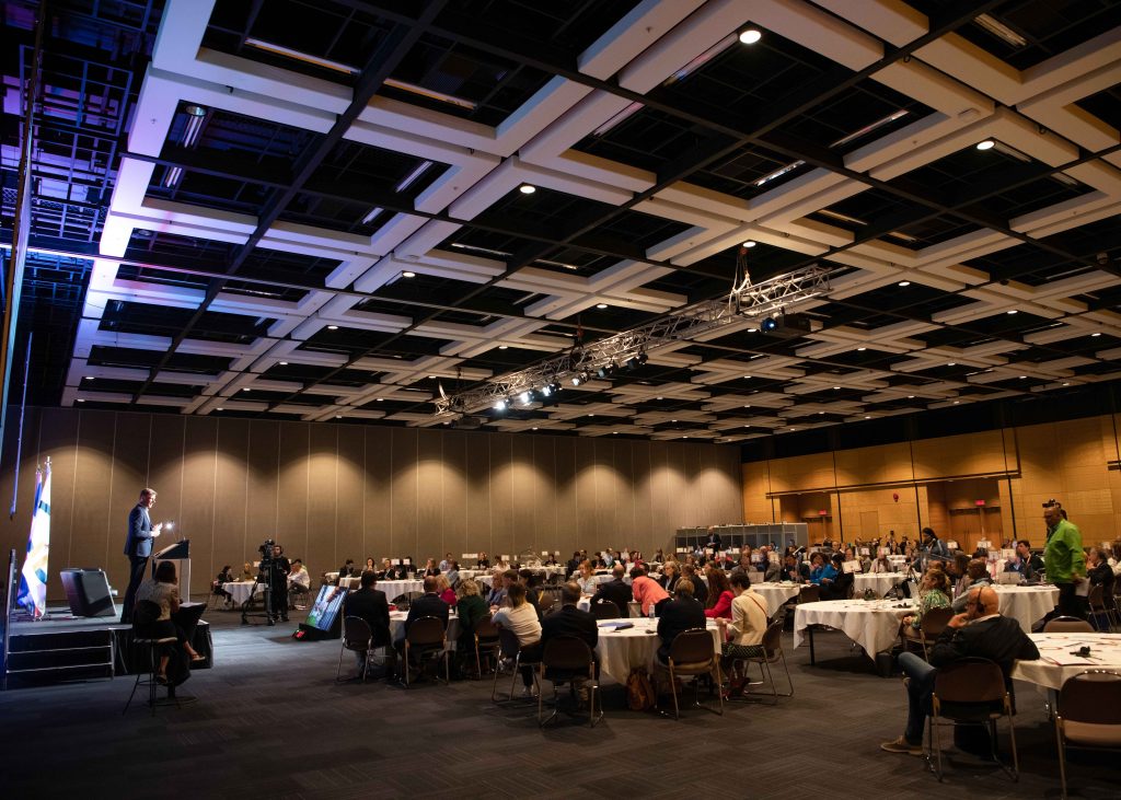 Congressistes autour de tables rondes pour banquets qui écoutent un conférencier sur la scène.