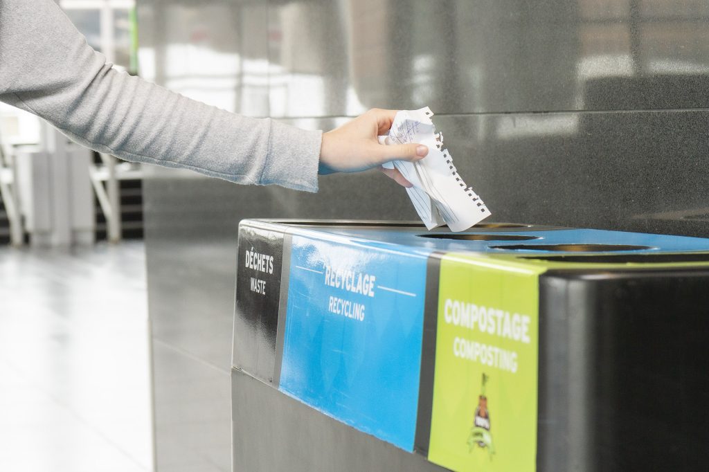 Bras d'une femme mettant ses papiers dans un ilôt multimatière, pour le recycler.