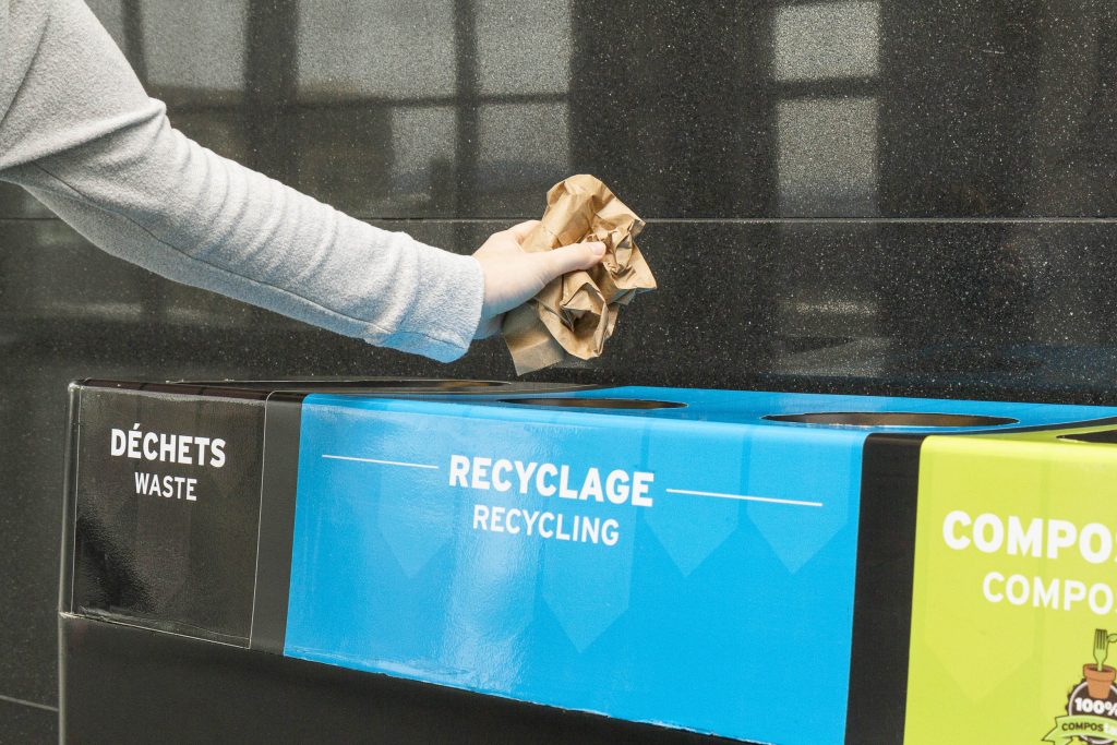 Bras d'une femme mettant ses papiers dans un ilôt multimatière, pour le recycler.