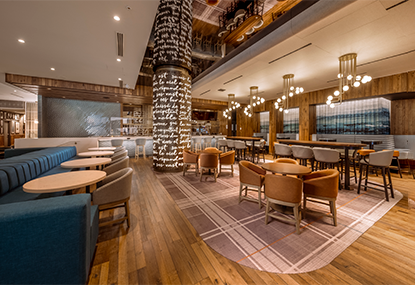 Photo of the CABU restaurant at the Hilton Québec, featuring a large blue sofa and beige chairs, as well as small round tables.