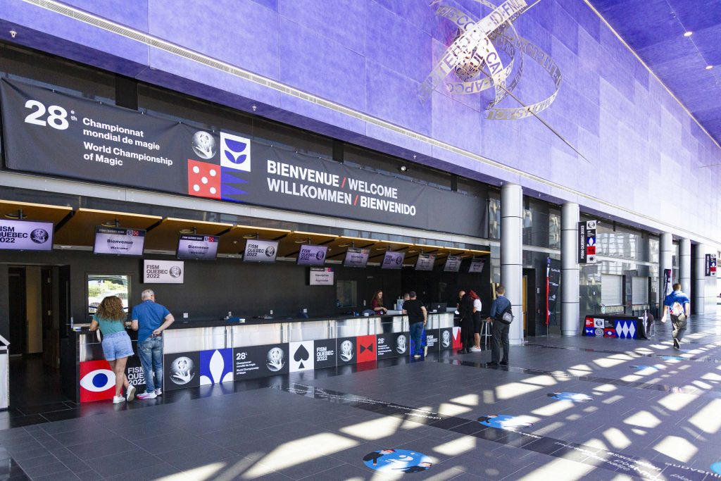 Main hall and registration desk at the Convention Centre during the World Championship of Magic. People are standing under a large banner waiting to register.