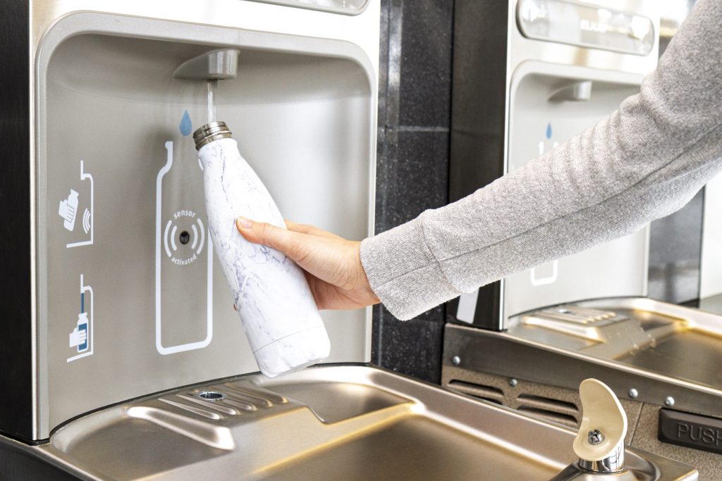 Bras de femme utilisant une des fontaines pour les gourdes du Centre des congrès. Elle tiens sa bouteille réutilisable pour la remplir.