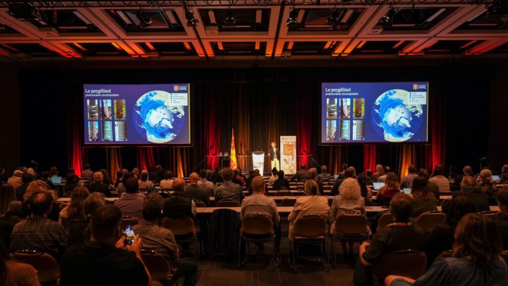 A convention hosted by Université Laval at the Québec City Convention Centre. A speaker presents on stage to a large seated audience, with dual screens displaying visuals about permafrost as a circumpolar phenomenon. The presentation includes Earth imagery and research data, highlighting academic engagement in climate science.
