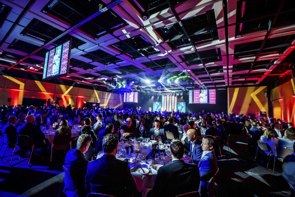 Belle salle illuminée d'orange, bleu et mauve avec des gens à table pour un banquet, lors du Gala des Fidéides.