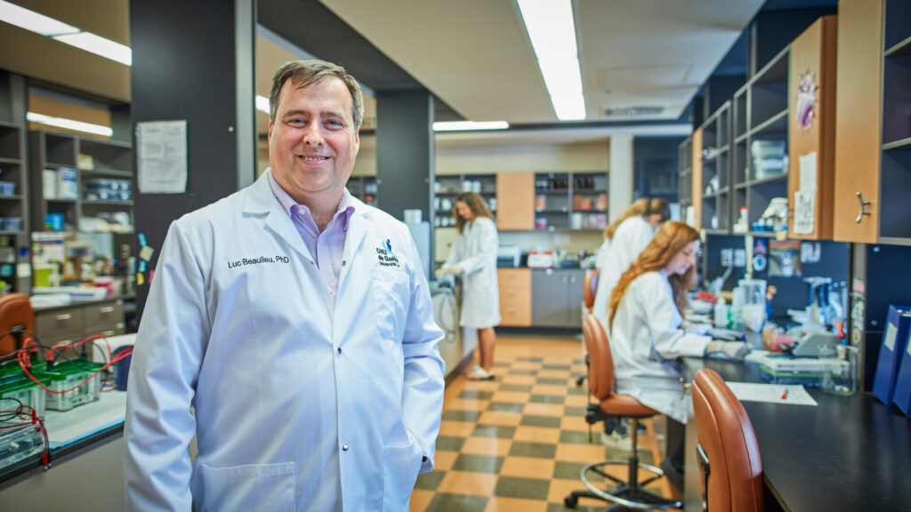 Researcher Luc Beaulieu standing in his laboratory at the CHU de Québec Research Centre, while other researchers are working in the background.