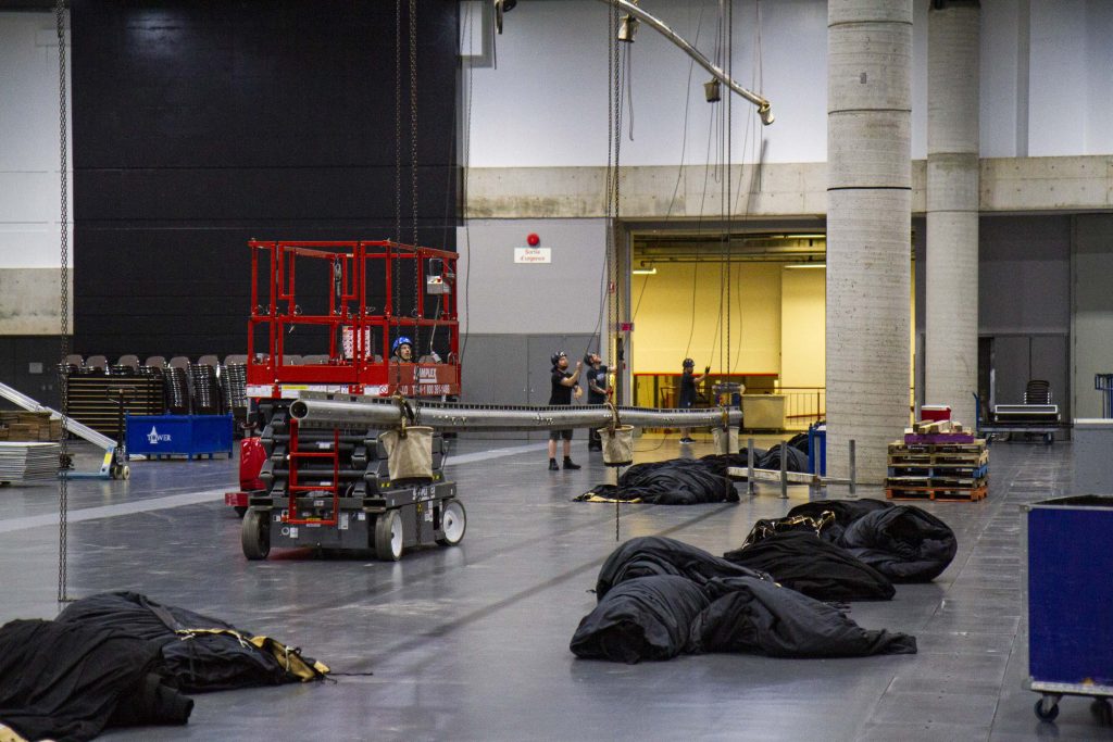 Salle en montage pour le Championnat de magie FISM 2022 où l'on peut voir l'installation de grands rideaux noirs à l'aide d'un chariot élévateur et de ponts d'accrochage.