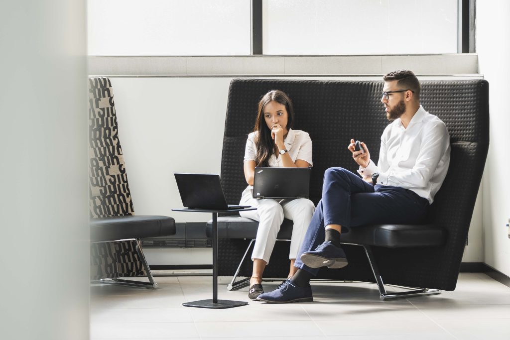 Deux jeunes professionnels qui discutent sur une banquette avec leur ordinateurs portables.