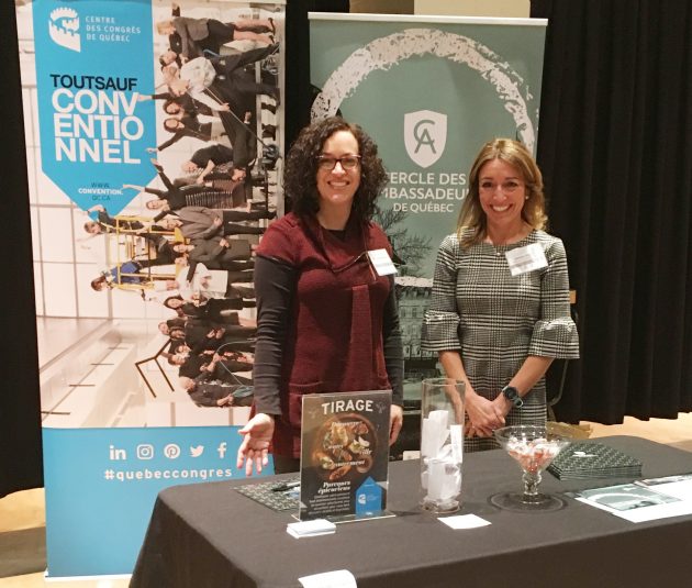 Photo of 2 women standing behind a table with posters of the Québec City Convention Centre and the Québec City's Ambassadors' Club behind them.