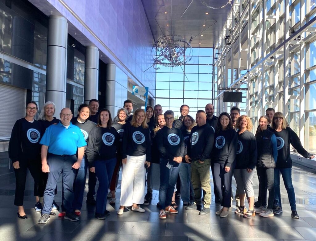The Québec City Convention Centre team members posing in the main lobby while wearing their team shirts in the Convention Centre’s signature blue colors.