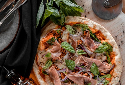 Gros plan d'une pizza cuite au four, au restaurant Piazzetta Saint-Jean, avec prosciutto, basilic et oignons rouges