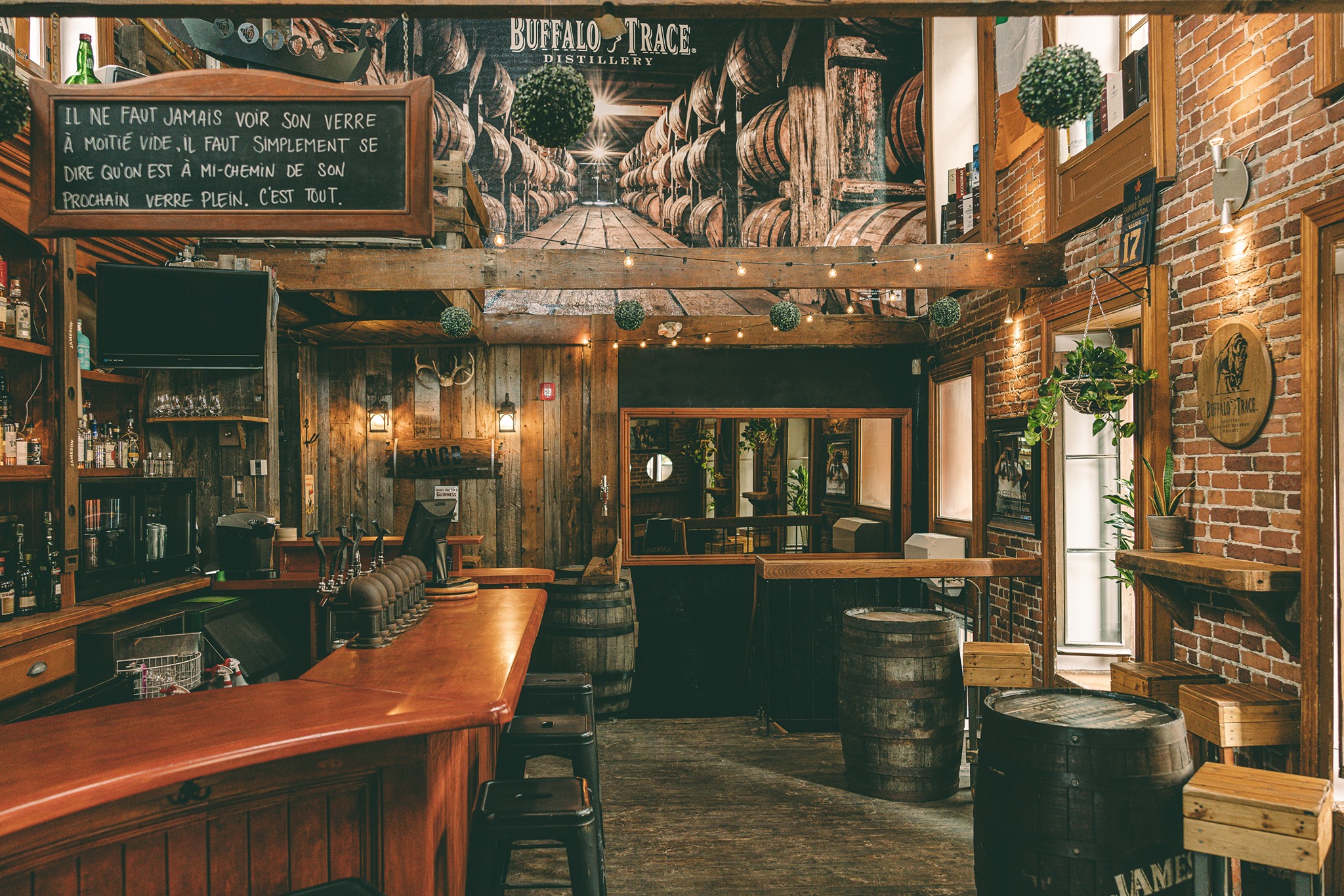Salle principale du bar Pub Nelligan's avec des tables hautes, des tabourets, un comptoir et un menu sur une ardoise.