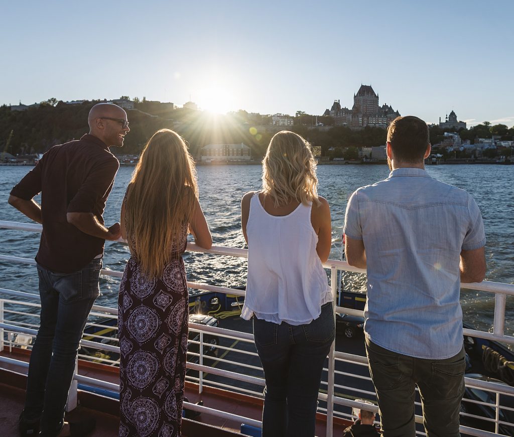 4 personnes de dos, sur le traversier Québec-Lévis qui regardent vers Québec. On voit bien le Château Frontenac.