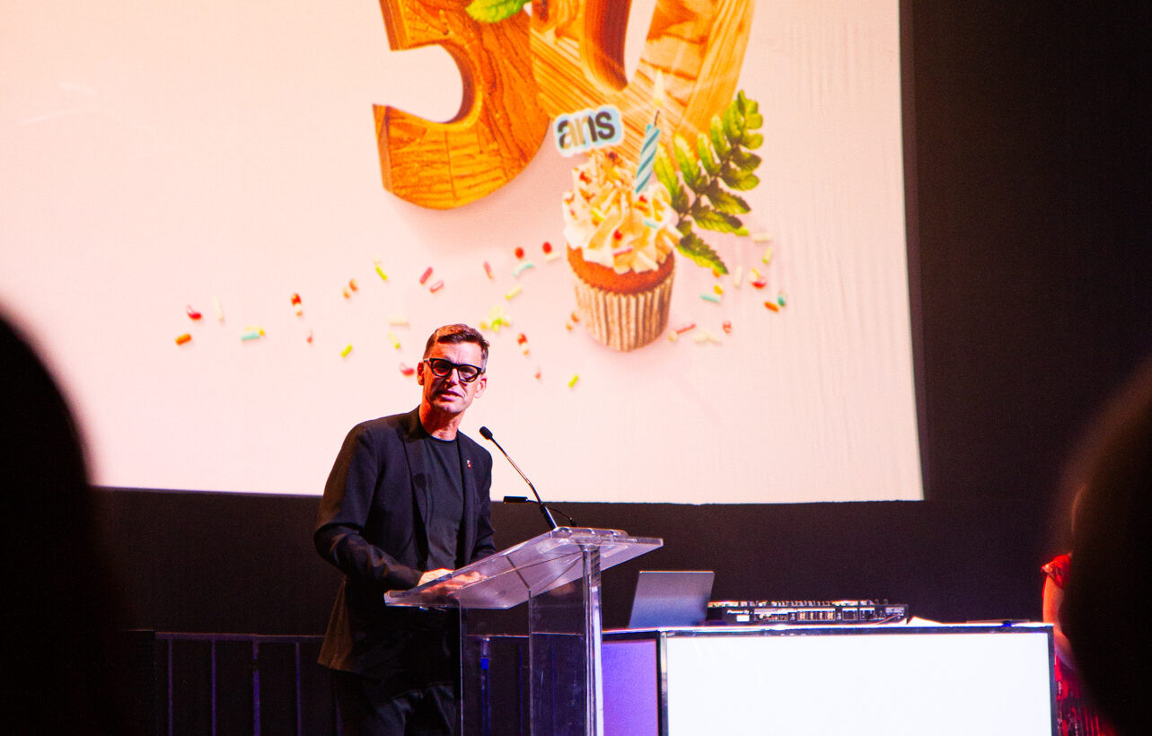 Québec City Mayor Bruno Marchand speaking on stage during the Québec City Convention Centre’s 30th anniversary gala, in front of a screen featuring the colours of the 30th anniversary celebrations.