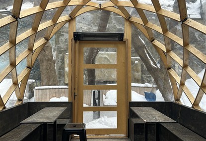 Terrasse intérieure du bar Sacrilège, avec des bancs et des tables mais la terrasse est vide et les fenêtres laissent apercevoir le dehors enneigé.