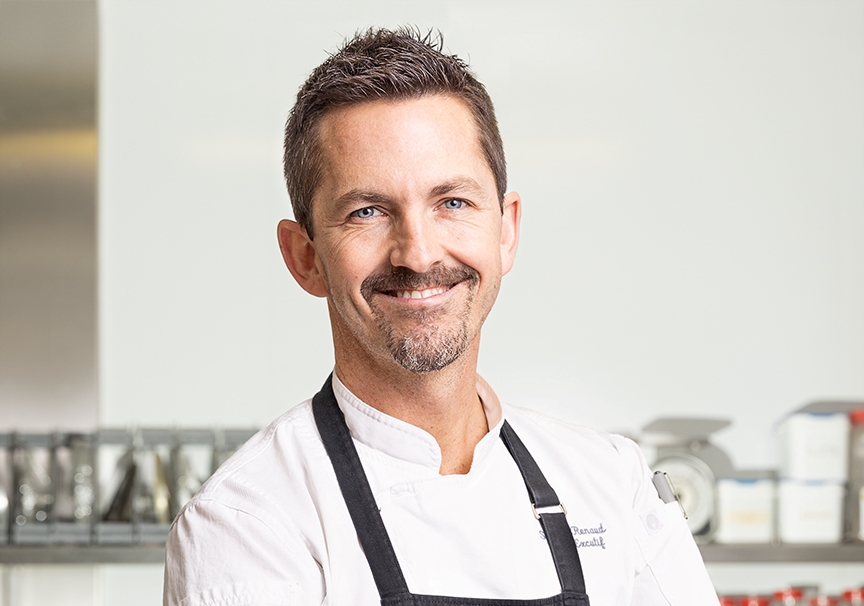 Portrait du chef Simon Renaud dans les cuisines du Centre, portant son uniforme et faisant un sourire à la caméra.