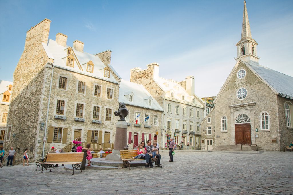 Église et grandes maisons de Place Royale, avec des gens qui visitent.