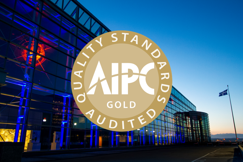Gold AIPC Quality Standards 2026 logo overlaid on a photo of the Québec City Convention Centre’s exterior façade, illuminated in blue at dusk.