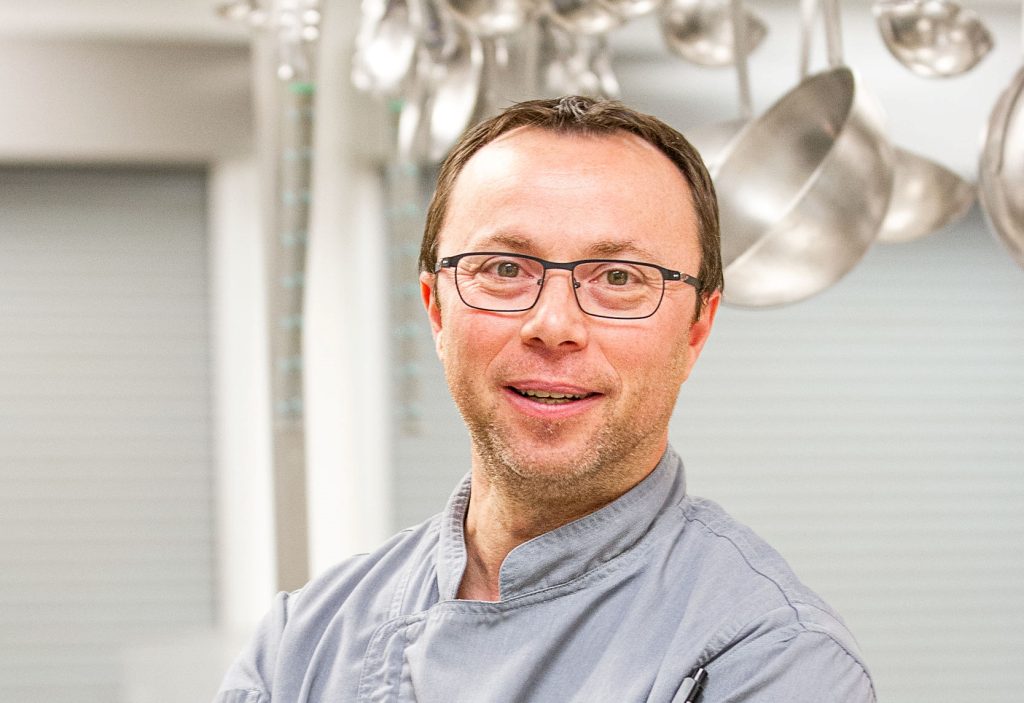 Portrait of Pastry Chef Vincent Coulange Renaud in the Centre's kitchens, wearing his uniform and smiling at the camera.
