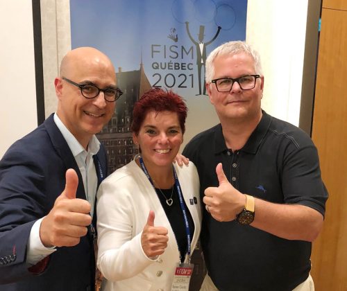 2 men and 1 women doing a thumbs up with a poster of FISM Québec 2021 in the background.