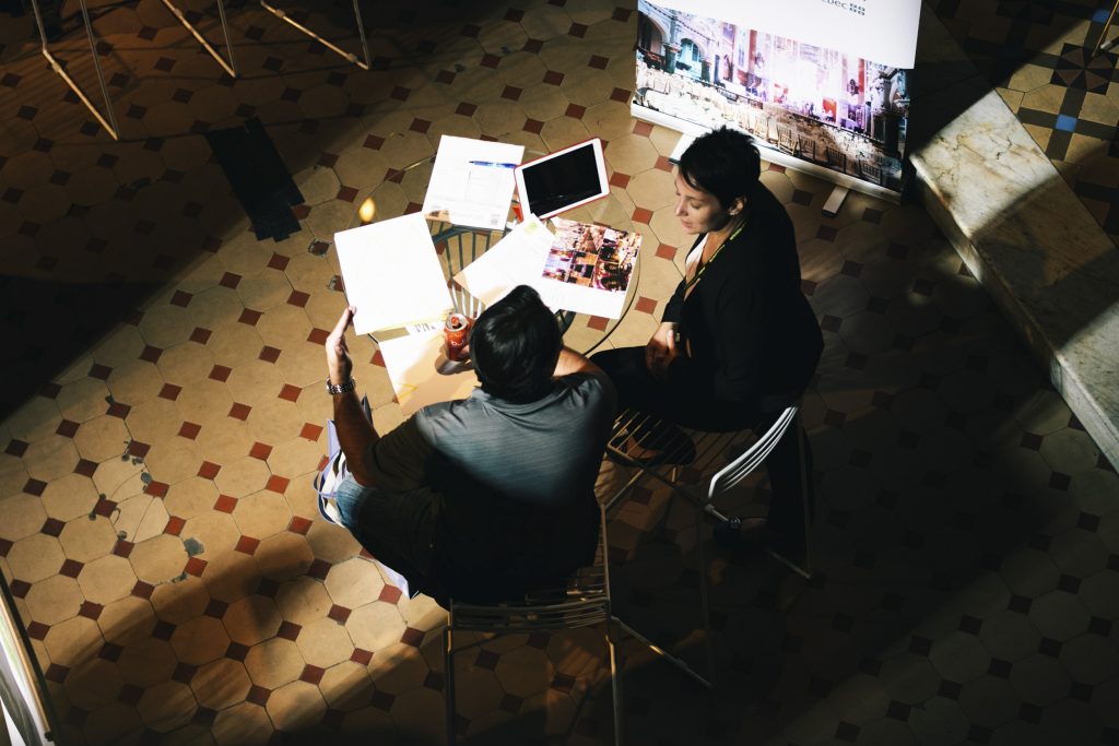 A man and a woman sitiing at a table with papers on the table.