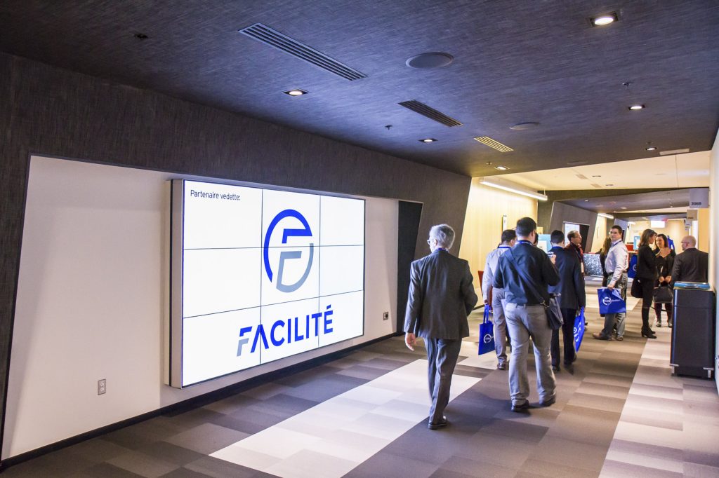 Hallway on the Convention Centre 3rd floor with attendees walking about and large screen on wall.