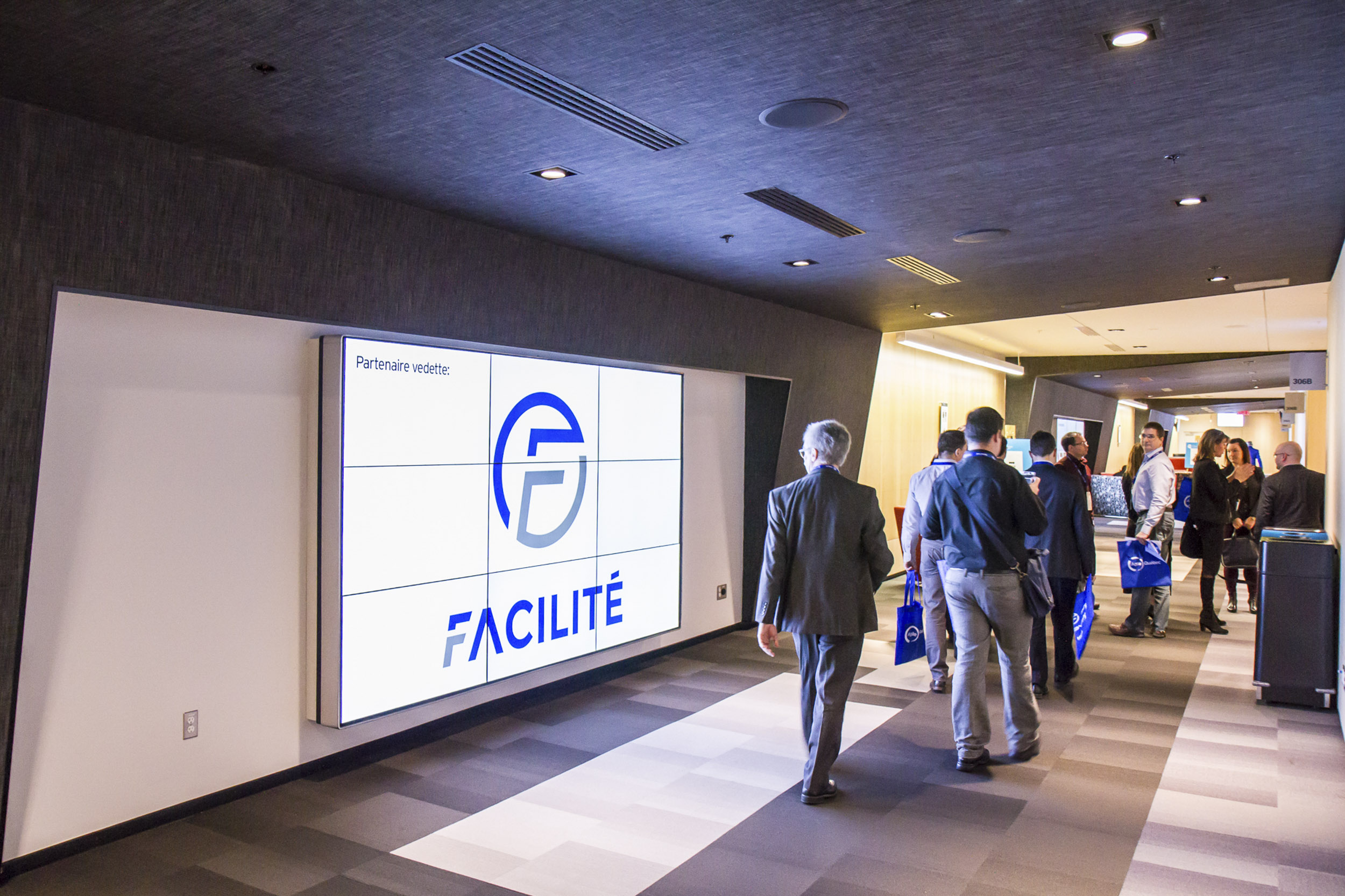 Congressistes qui passent devant une murale vidéo dans le Foyer 306.