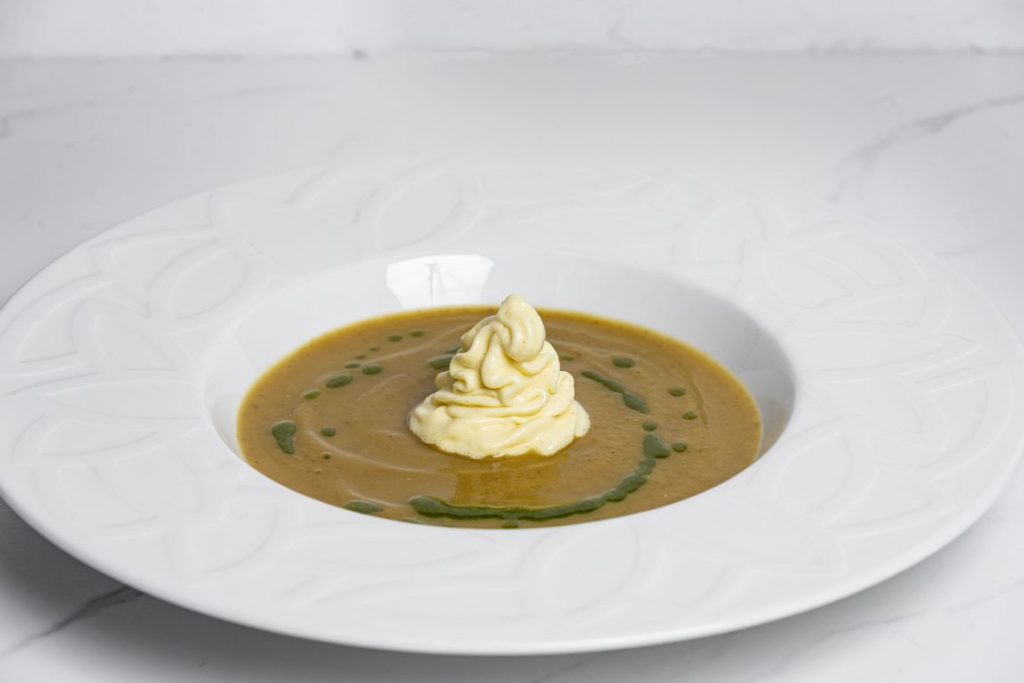 Bol de soupe à la citrouille et au miso, avec une crème au milieu et une huile aromatisée comme garniture.