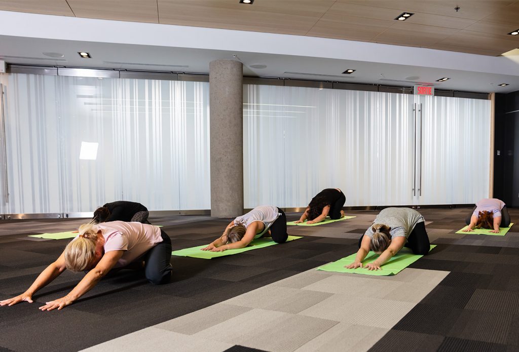 Women doing yoga on green mats, placed on top of dark carpet, in the Québec City Convention Centre's anything but conventional event sector.