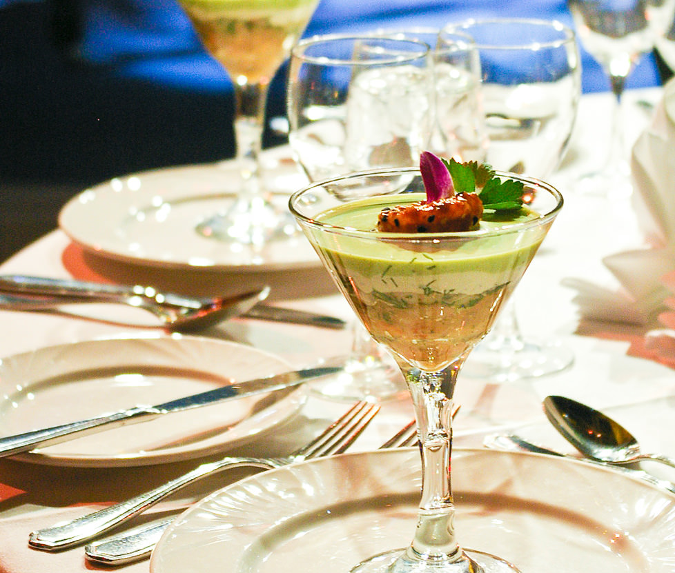 Coupe de style martini, remplie d'un étagé de mousse de saumon fumé, de crème sûre et d'une guacamole. Le tout est décoré d'une crevette marinée et d'une fleur comestible.