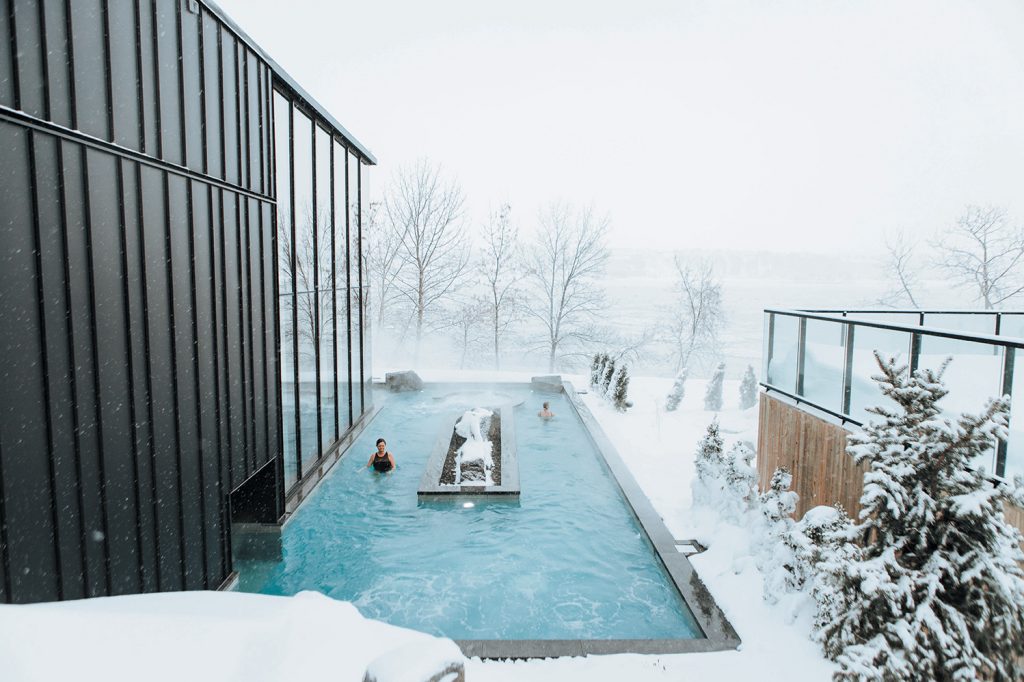 Deux personnes dans une piscine chaude du Strom Spa, avec de la neige et les arbres autour.