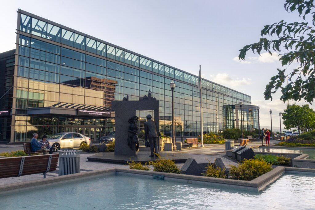 Exterior façade of the Québec City Convention Centre in summer, featuring the fountains and greenery of Promenade Desjardins.