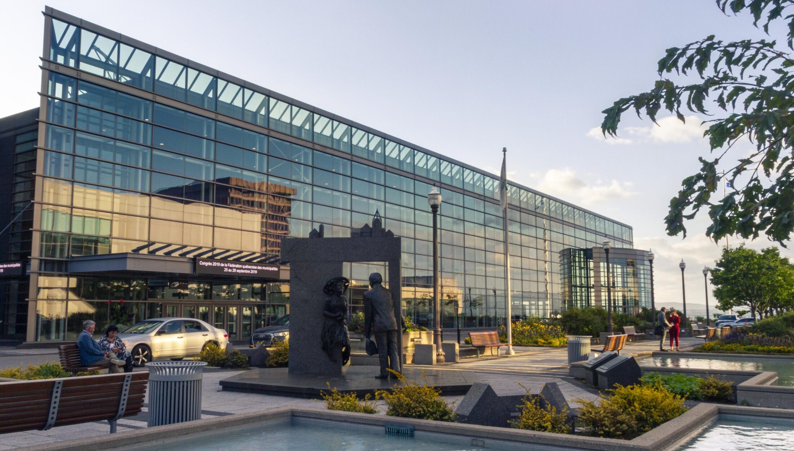 Exterior façade of the Québec City Convention Centre in summer, featuring the fountains and greenery of Promenade Desjardins.